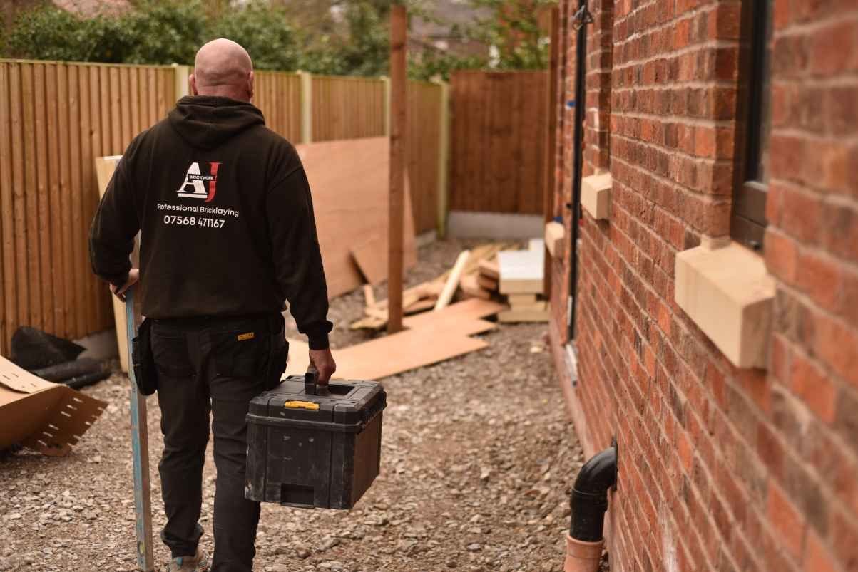 AJ Brickwork bricklayer carrying tools alongside new brickwork on a Manchester house extension
