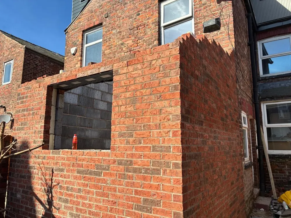 Extension wall built in reclaimed red brick with a window opening and toothed brickwork